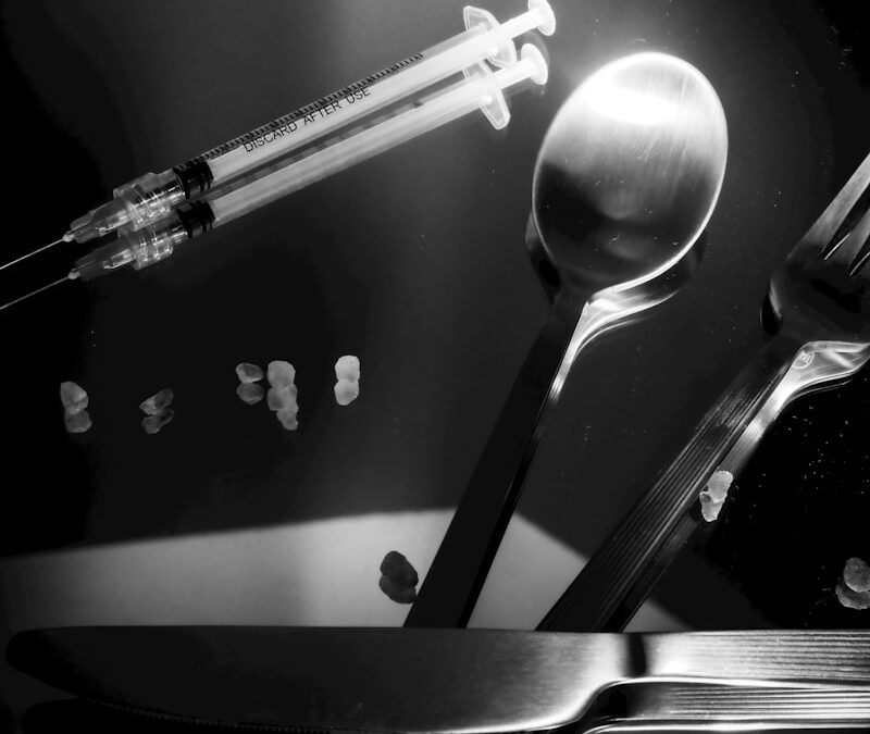 Syringes and cutlery on a reflective surface.